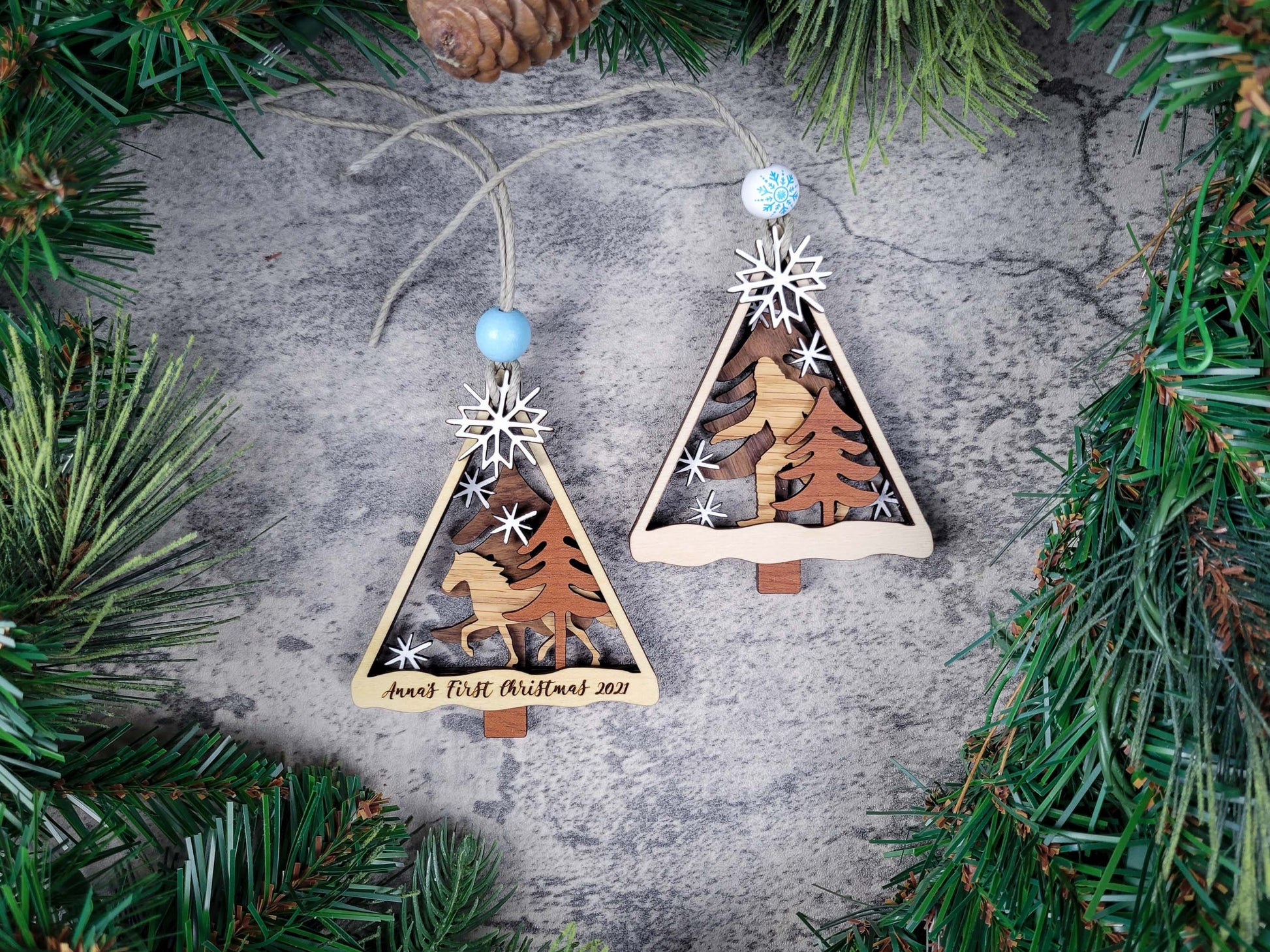 Wooden Christmas tree ornaments with animal designs on a textured surface surrounded by greenery.