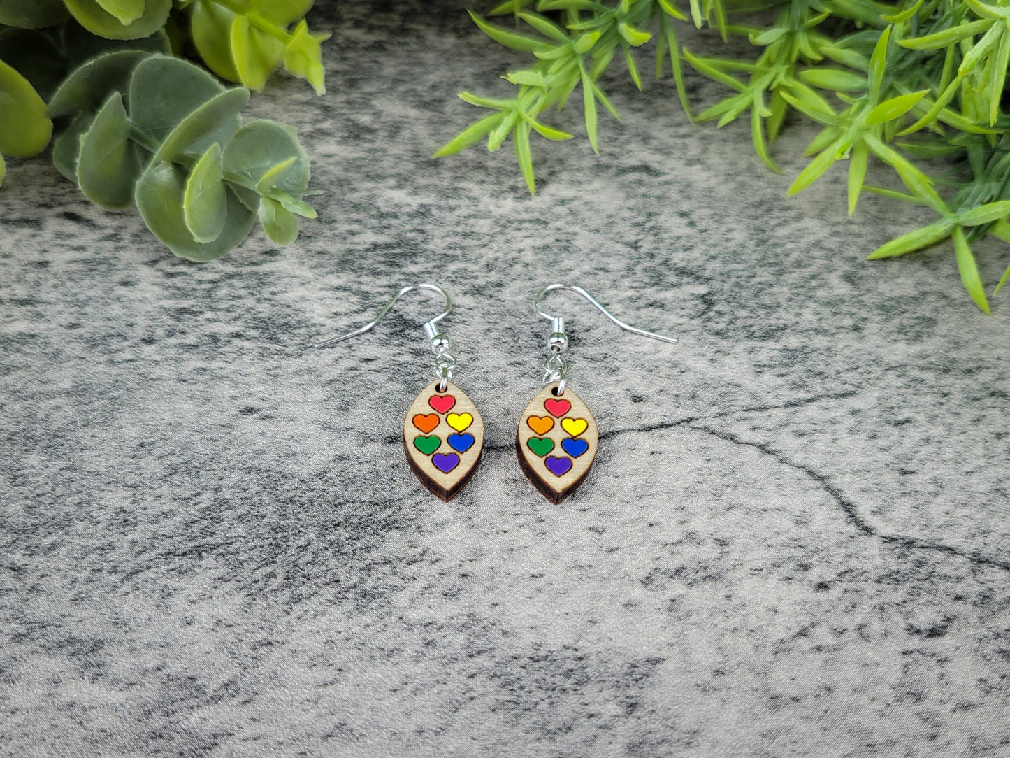 Colorful heart-shaped earrings on a gray stone surface with green leaves in the background