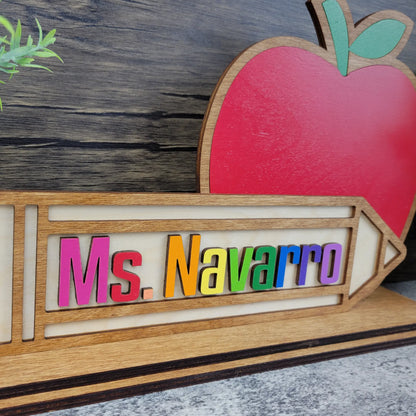 Wooden nameplate with 'Ms. Navarro' and a red apple on a wooden background